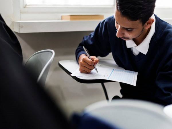 Como usar a nota do ENEM: jovem em uma sala de aula, sentado em uma cadeira e fazendo uma prova