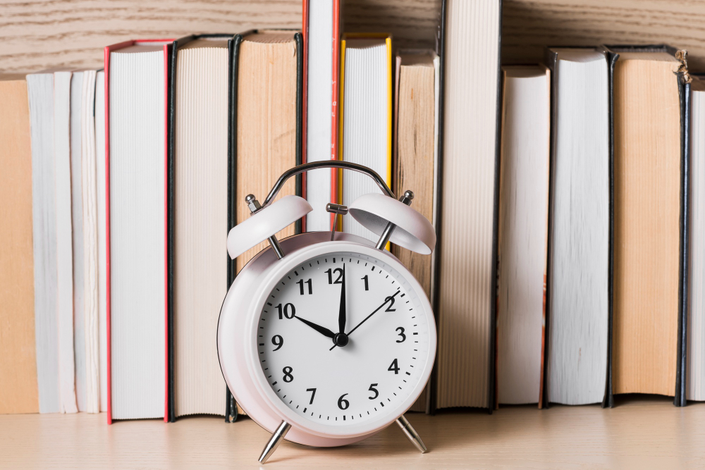 Relógio de mesa na frente de alguns livros enfileirados, representando a gestão do tempo durante os estudos